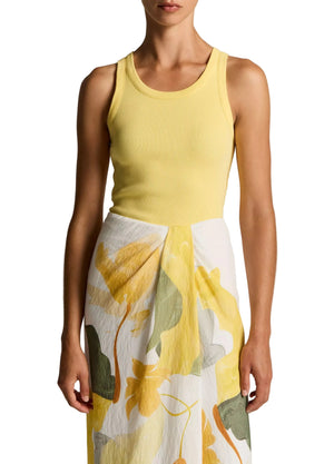 A woman wearing the Vince Ribbed Scoop Neck Tank, a sleeveless yellow finely ribbed top crafted from a soft cotton-modal blend, paired with a white skirt featuring a yellow and green floral print, stands against a plain background.