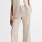A person stands against a plain background, wearing a beige pinstriped short-sleeve shirt, white top, brown sandals, and vince Low Rise Ticking Striped Crop Flare Trousers.