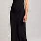 A person is wearing the vince Draped Funnel Neck Dress in black matte crepe, featuring a sleeveless design and pleated details, paired with light beige ankle boots, standing against a plain light background.