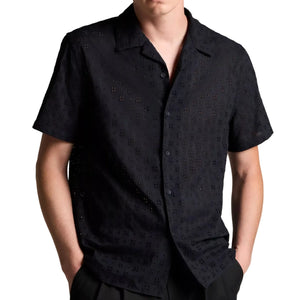 A man wears the Vince Cotton Eyelet SS Collar Shirt—a short-sleeve, black button-up shirt with a subtle eyelet pattern—standing with his hands in his pockets against a white background.