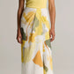 A woman wearing the Vince Ribbed Scoop Neck Tank in yellow, paired with a white midi skirt featuring yellow and green leaf prints and brown sandals, stands against a neutral background.
