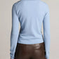 A person is shown from the back against a neutral background, wearing the Vince Long Sleeve High V-Neck Polo Sweater in light blue and dark brown leather pants.