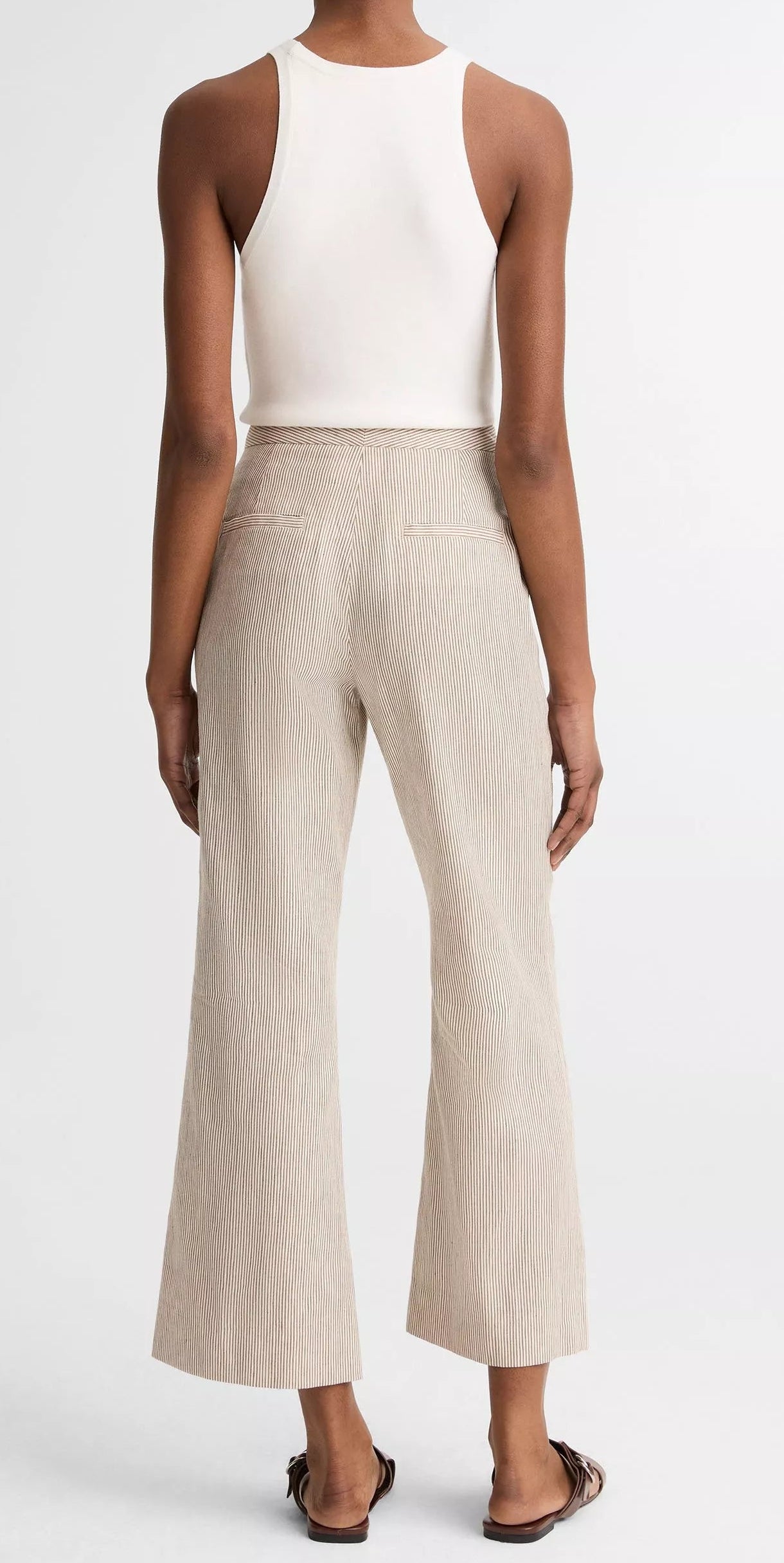 A person faces away, wearing a white sleeveless top, vince Low Rise Ticking Striped Crop Flare Trouser, and sandals.