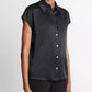 A person wearing the vince Cap Sleeve Silk Blouse—a slim fit, short-sleeved black silk button-up top with a collar—paired with black pants, stands against a plain white background.