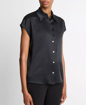 A person wearing the vince Cap Sleeve Silk Blouse—a slim fit, short-sleeved black silk button-up top with a collar—paired with black pants, stands against a plain white background.