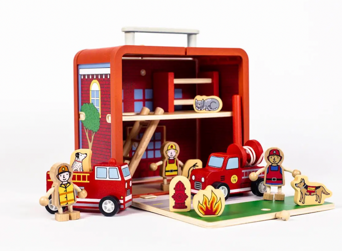 The Jack Rabbit Creations Suitcase Series unfolds into a wooden fire station playset with miniature firefighters, fire trucks, a hydrant, and a Dalmatian.