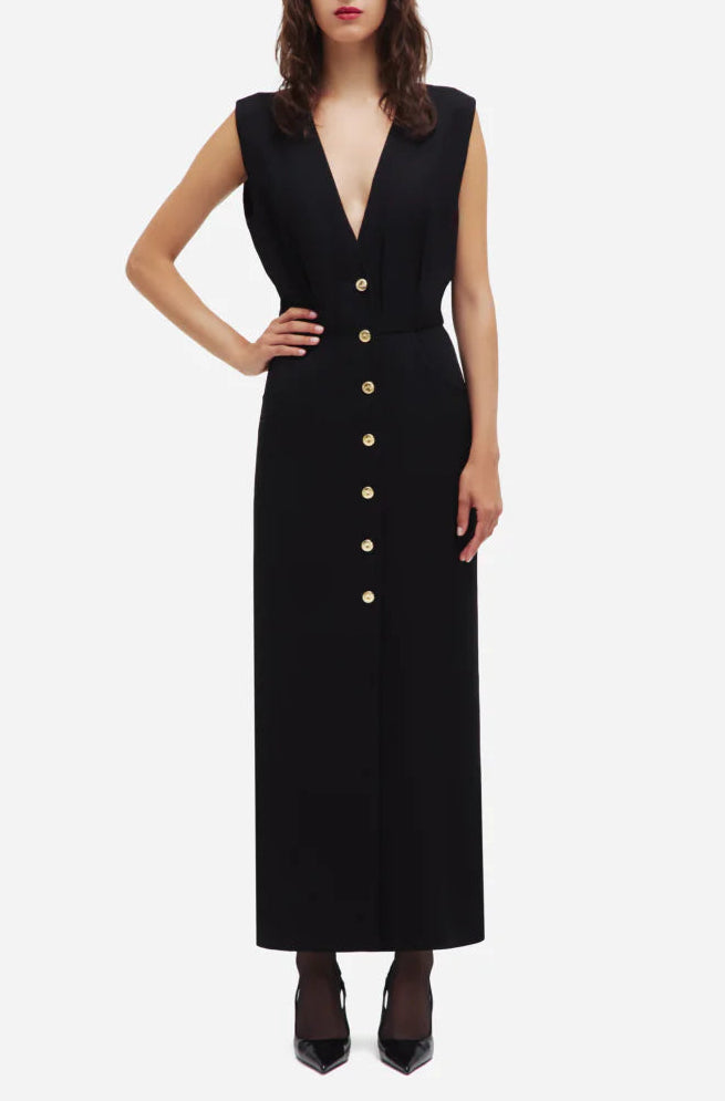 Woman wearing the Luna Friesian Long Dress by Blaze Milano—sleeveless, black, long, with a deep V-neck and gold-tone buttons, standing with one hand on her hip.