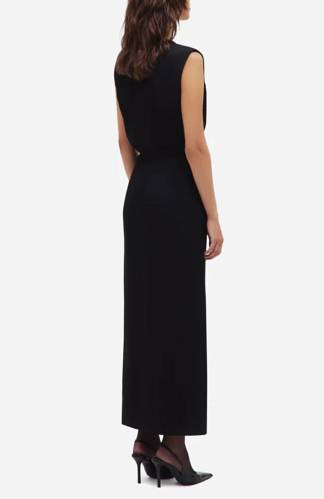 A woman faces away, wearing the Luna Friesian Long Dress by Blaze Milano—sleeveless, black with gold-tone buttons—and black heels against a white background.
