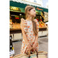 A young girl wearing the Louis Louise Girls’ Arlette Dress holds a woven bag while standing in front of a fruit market stall outdoors.