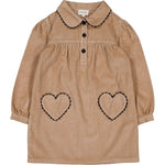 The Girls' Belinda Big Corduroy Dress by Louis Louise features long sleeves, a tan corduroy design, Peter Pan collar, black buttons, and two heart-shaped pockets outlined in black stitching.
