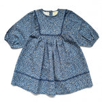 The Louis Louise Girls’ Mahana Dress is a blue long-sleeve denim dress with a loose fit, a gathered waist, decorative seam details, and an all-over leopard print pattern. It features a round neckline for added style.