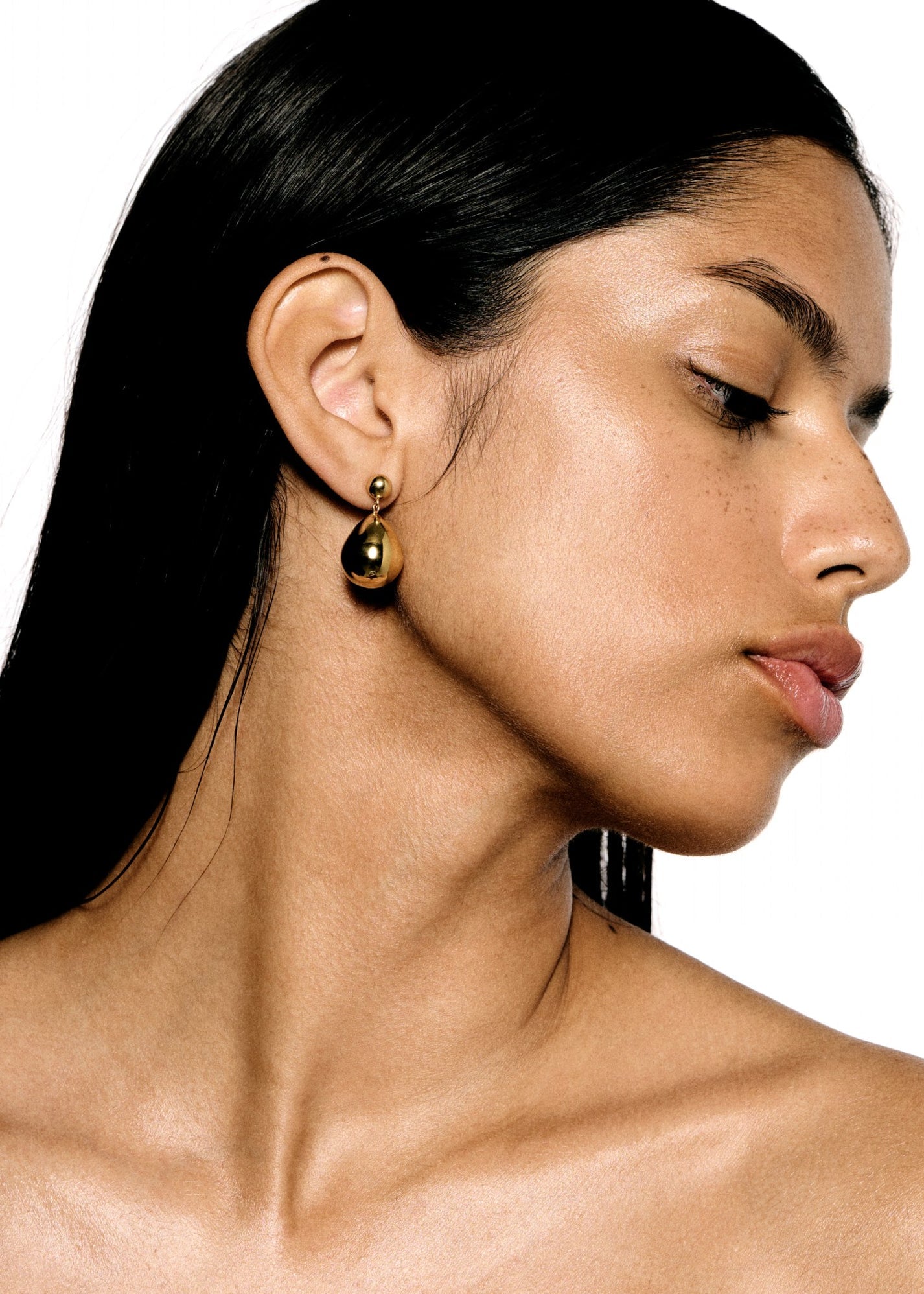 A woman with long dark hair wears a pair of LIÉ STUDIO Julie Earrings from Lie Studio. She is facing the camera's right side. The background is plain white.