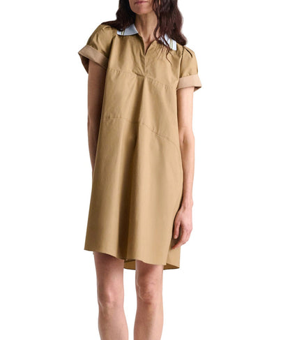 A woman stands against a plain white background wearing the Dorothee Schumacher Poplin Power Mini Shirt Dress, a loose-fitting, short-sleeve A-line dress in tan cotton poplin with a crisp white collar.