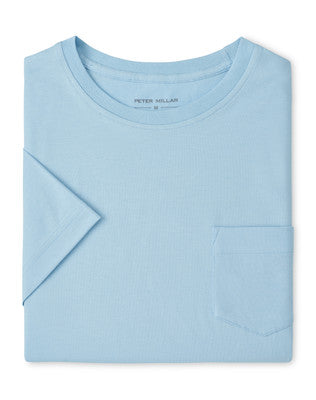 The Peter Millar Crown Comfort Pocket Tee, a light blue short-sleeve shirt crafted from soft organic cotton with a chest pocket, is neatly folded and displayed on a plain white background.