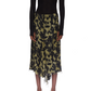A person is seen from the front wearing a long-sleeve black top and the Victoria Beckham Corset Detail Skirt—an olive green asymmetric midi skirt with a black floral pattern.