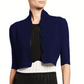 A person wearing the Lela Rose Scallop Trim Knit Bolero in navy blue over a black and white textured dress, shown from shoulders to waist.