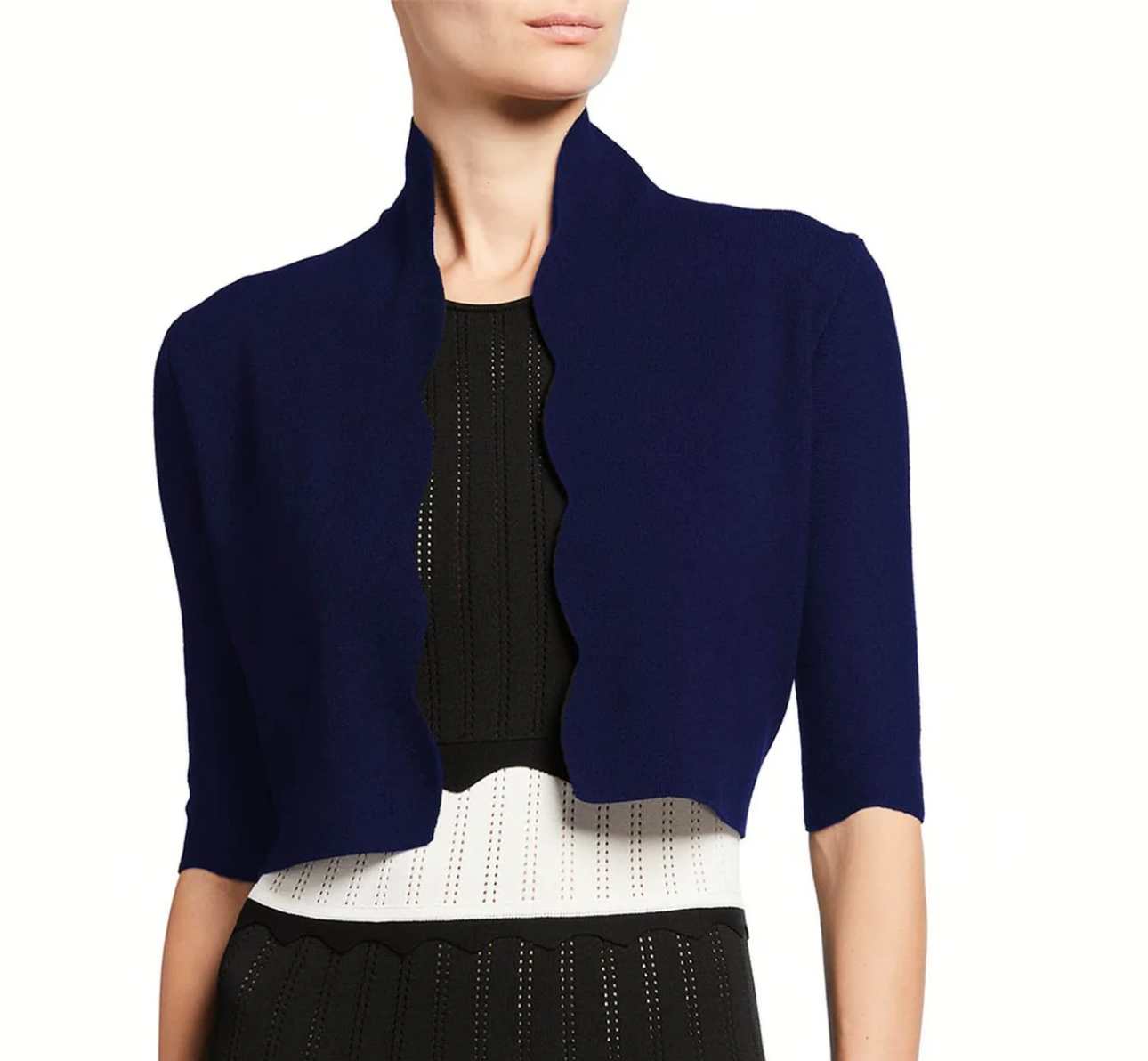 A person wearing the Lela Rose Scallop Trim Knit Bolero in navy blue over a black and white textured dress, shown from shoulders to waist.