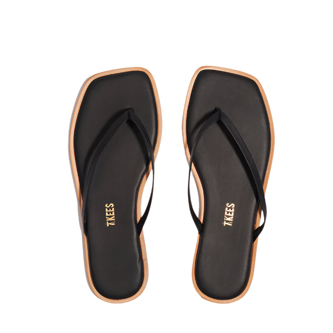 A pair of Tkees Dylan Sandals for women in black with square toes and tan soles, handcrafted from Brazilian leather, shown from above on a white background.