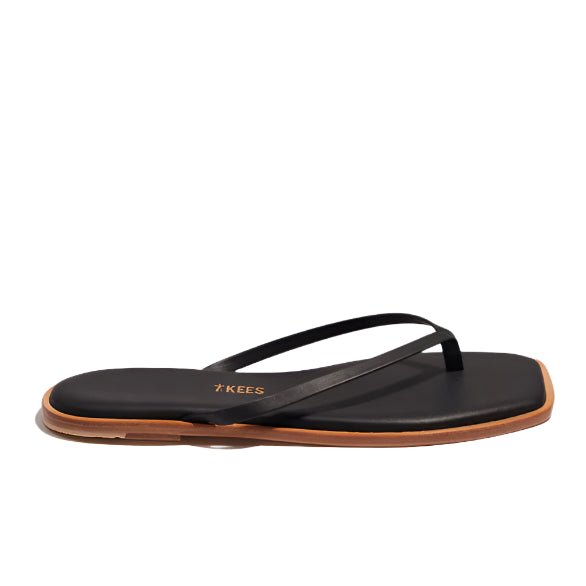 A side view of the Tkees Dylan Sandal, a handcrafted black flip flop with a tan sole, displayed on a white background.