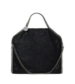 The Stella McCartney Falabella Fold Over Tote is a black, rectangular vegan bag made from recycled plastic bottles, featuring a metallic chain handle and trim with a slight sheen, shown against a white background.