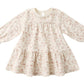 The Quincy Mae Baby Girls' and Girls' Tiered Jersey Dress features long sleeves, a cream color with a light pink floral pattern, a ruffled skirt, and gathered cuffs.
