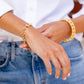 Wearing a white shirt and blue jeans, someone adjusts their Juliska Capucine De Wulf Berry Clover Linear Bracelet, with a stylish stack adorning the other wrist.