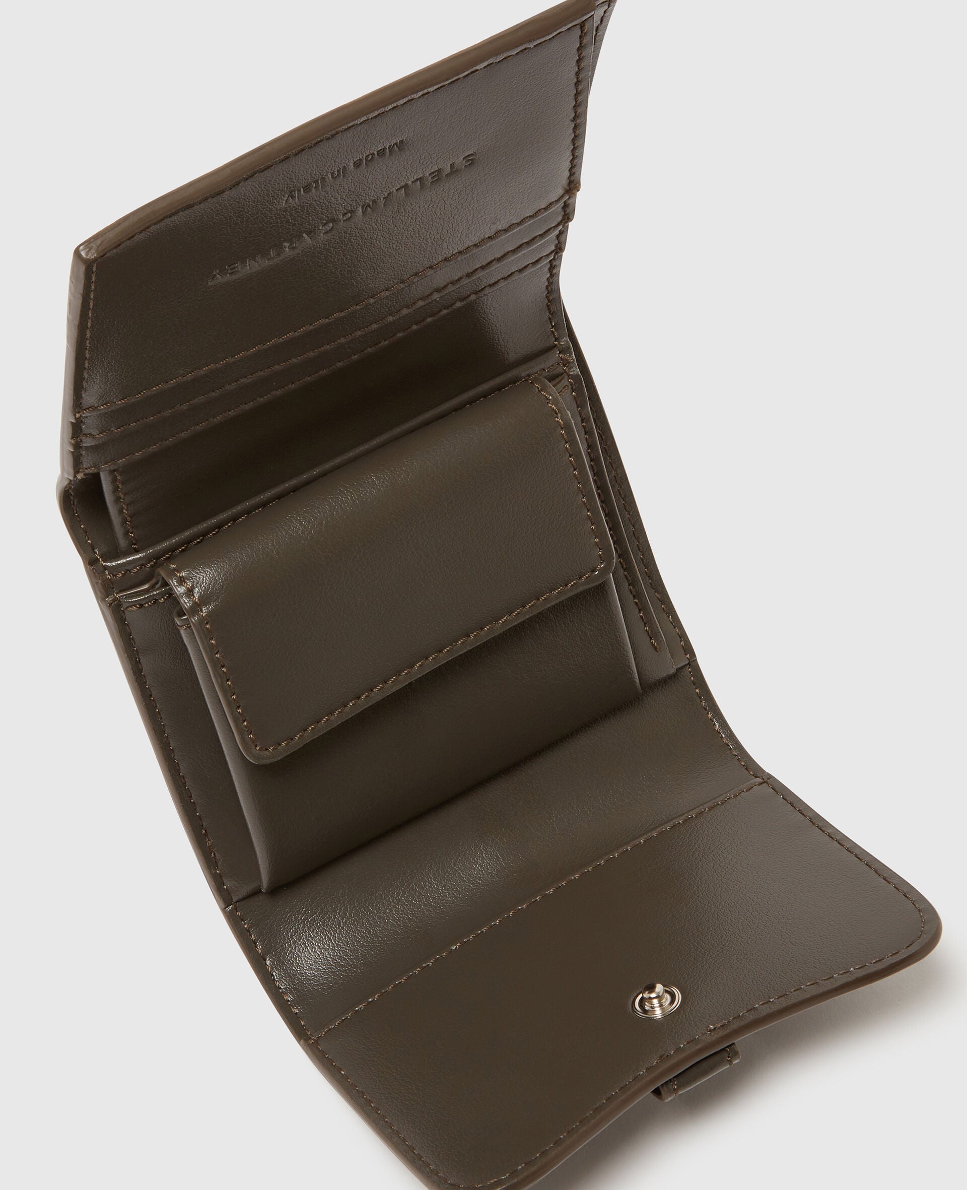 The Stella McCartney Ryder Trifold Wallet is an open brown leather wallet with multiple compartments and a snap button closure, handcrafted in Italy and shown against a plain background.