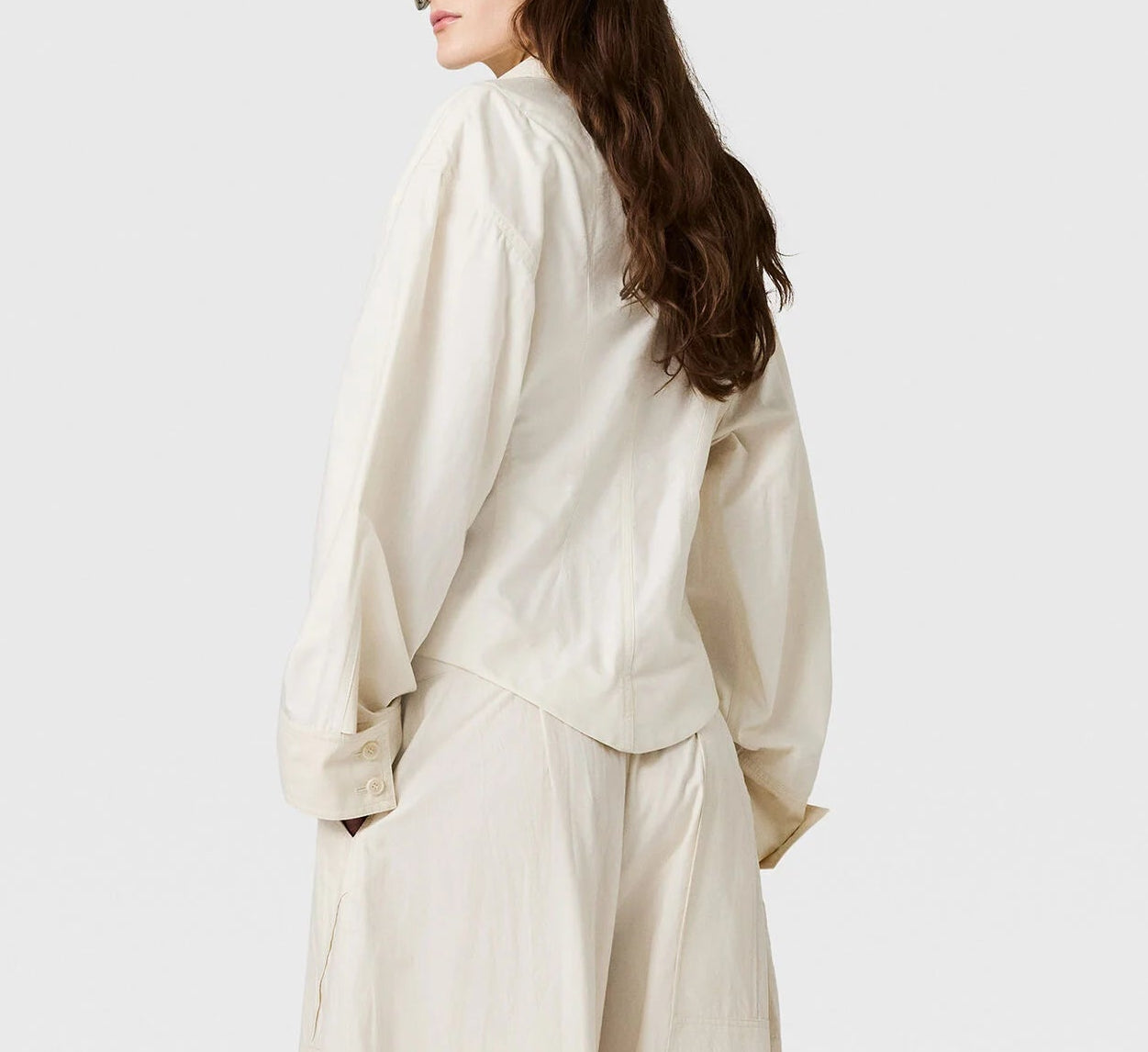 A person with long brown hair, seen from behind against a plain background, wears Stella McCartney’s oversized Washed Cotton Utility Top in cream with matching loose pants.