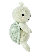 The Kelp Green Sea Turtle - Baby 7" from Cuddle + Kind is a hand-knit plush turtle made from heirloom-quality Peruvian cotton yarn, featuring a light green shell, cream-colored body, black stitched eyes, and a small tuft of yarn on its head for lasting softness and charm.