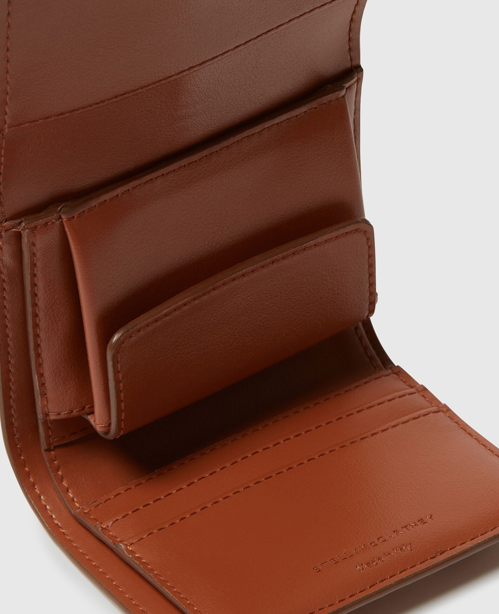 Open brown leather Ryder Trifold Wallet by Stella McCartney, displaying card slots, a coin pouch, and part of the debossed logo inside—an elegant accessory expertly handcrafted in Italy.