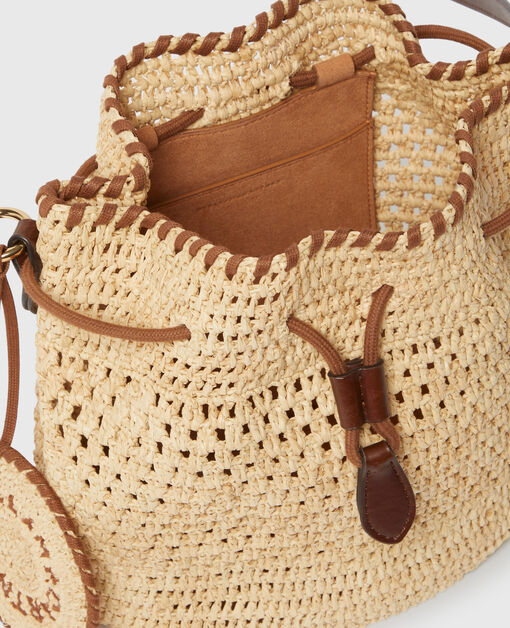 A close-up of the Stella McCartney Falabella Crochet Raffia Bucket Bag with brown leather trim, highlighting its drawstring closure and inner pocket—showcasing luxury vegan craftsmanship.