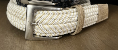 Close-up of three Men's Solid Stretch Belts by W. Kleinberg stacked on wood: the top one is black and white, the middle is white and beige, and the bottom is vibrantly colored. Each belt showcases a silver buckle with elegant crocodile tabs for added style.