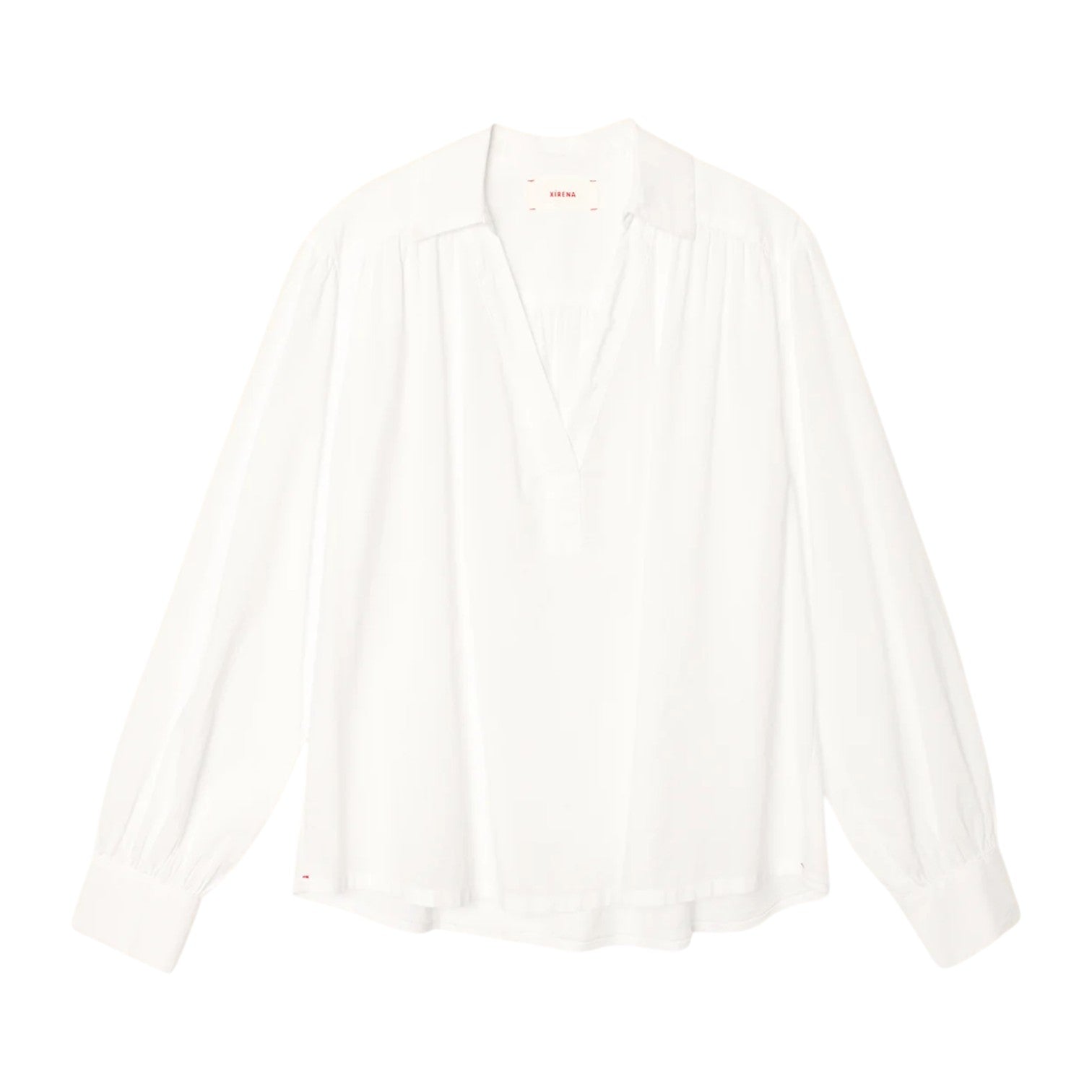 The Elena Top by Xirena is a loose-fitting, long-sleeve white popover with a Johnny collar and V-neck, made from lightweight cotton poplin, shown against a plain white background.