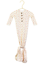The Lou Lou & Company Baby Girls’ Lottie Knotted Gown, displayed on a hanger, is a white baby gown with a small red floral pattern. It features long sleeves, a button-down front for easy dressing, and a knotted tie-bottom design that simplifies diaper changes.