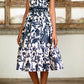 A person in an Andres Otalora Encanto Midi Dress with a classic feminine silhouette stands before a decorative wooden panel, wearing brown sandals.