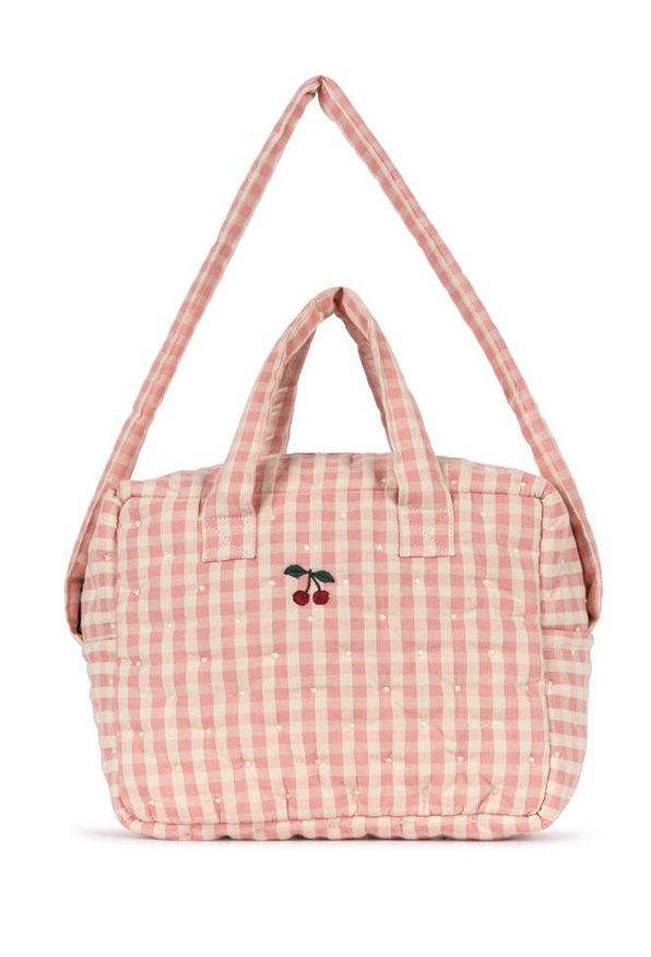 The Konges Slojd Doll Bag is a checkered pink bag with cherry embroidery. It features a large pocket, long shoulder strap, and two short handles, perfect for stylish doll parents as a changing bag.