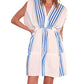 Woman wearing a white, hand-woven cotton lemlem Alem Plunge Dress with vertical blue stripes. The short dress has a V-neck and a gathered waist, perfect for resort wear. She is standing with one arm on her hip.