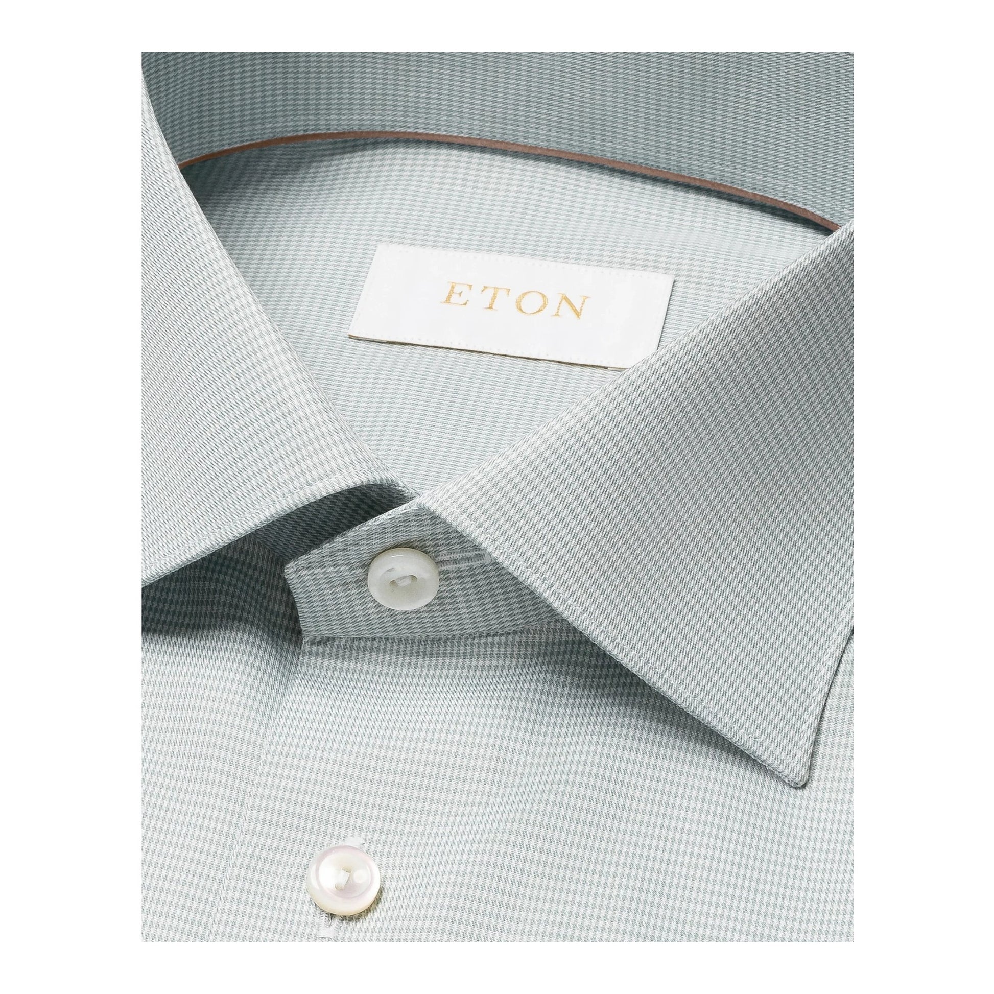 Close-up of a mid green houndstooth elevated twill shirt by Eton, featuring white buttons and a visible brand label inside the collar.