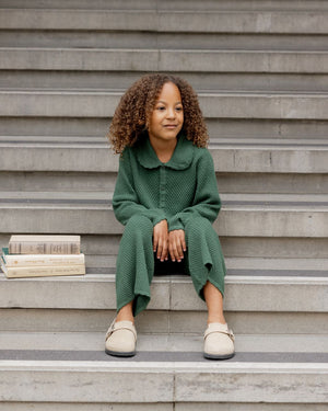 A young child in Rylee & Cru Girls' Knit Wide Leg Pants with a ribbed waistband sits on outdoor steps beside a small stack of books, gazing slightly to the side.
