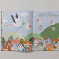 Pages from the charming children's book, *Write to Me Your Baby Story* by Write To Me, beautifully depict storks carrying bundles over a vibrant village. This delightful read is ideal for celebrating first birthdays. Storks glide above houses, hills, and trees while featuring an enchanting rhyming text.