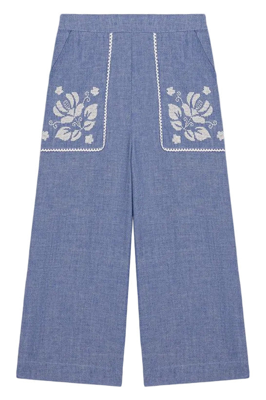 Louise Misha Girls’ Flofi Pants—wide-leg blue denim pants featuring white floral embroidery and lace trim on the front pockets, shown laid flat on a white background.