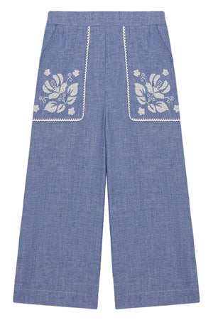 Louise Misha Girls’ Flofi Pants—wide-leg blue denim pants featuring white floral embroidery and lace trim on the front pockets, shown laid flat on a white background.