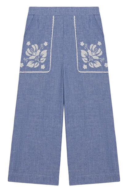 Louise Misha Girls’ Flofi Pants—wide-leg blue denim pants featuring white floral embroidery and lace trim on the front pockets, shown laid flat on a white background.