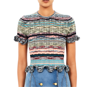A person wears the Ulla Johnson Miya Knit Top—a short-sleeve, multicolored striped space-dyed piece with ruffled edges—paired with high-waisted blue jeans accented by gold buttons.