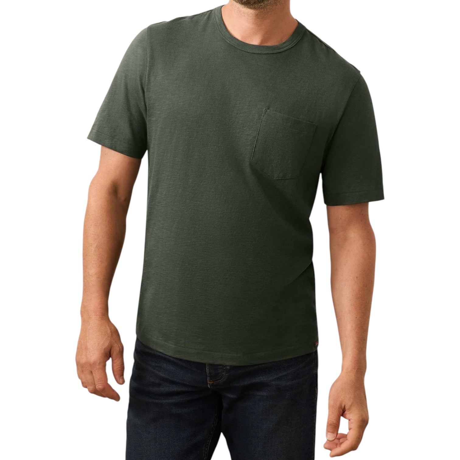 A man models the Faherty Sunwashed Pocket Tee in dark green with short sleeves and a chest pocket, paired with dark blue jeans, set against a white background to highlight its relaxed silhouette.