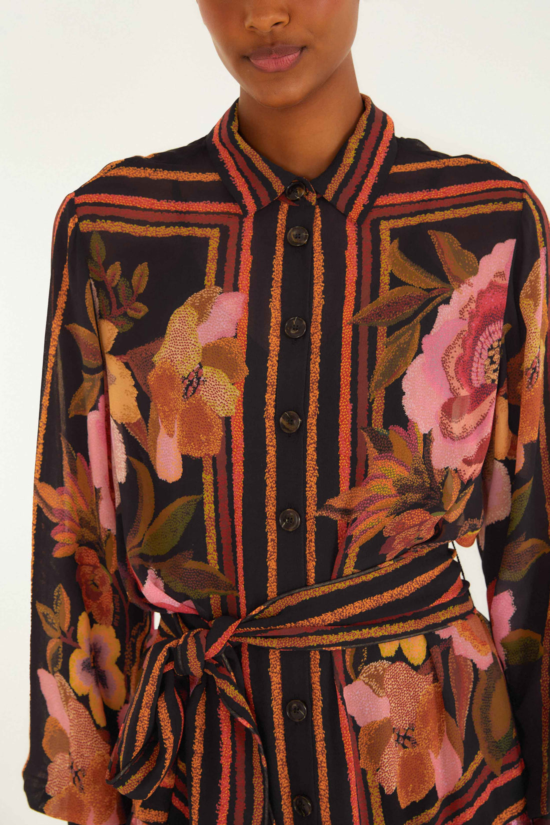 A person wearing the Farm Rio Chenille Flowers Black Mini Dress, a long-sleeved, belted dress featuring black, orange, and pink floral and striped patterns.