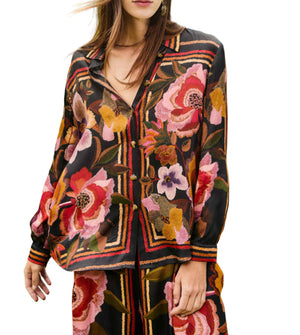 A woman wears the Farm Rio FR Chenille Flowers Black Shirt, a dark long-sleeved top with bold florals and geometric stripes, made from eco-conscious viscose and paired with matching pants.