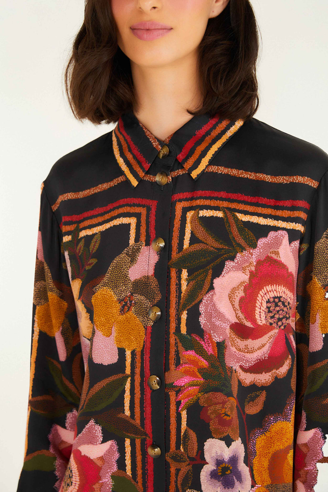 A woman wears the Farm Rio Chenille Flowers Black Shirt, a black button-up made from eco-conscious viscose featuring bold red, pink, orange, and yellow floral and geometric chenille embroidery.