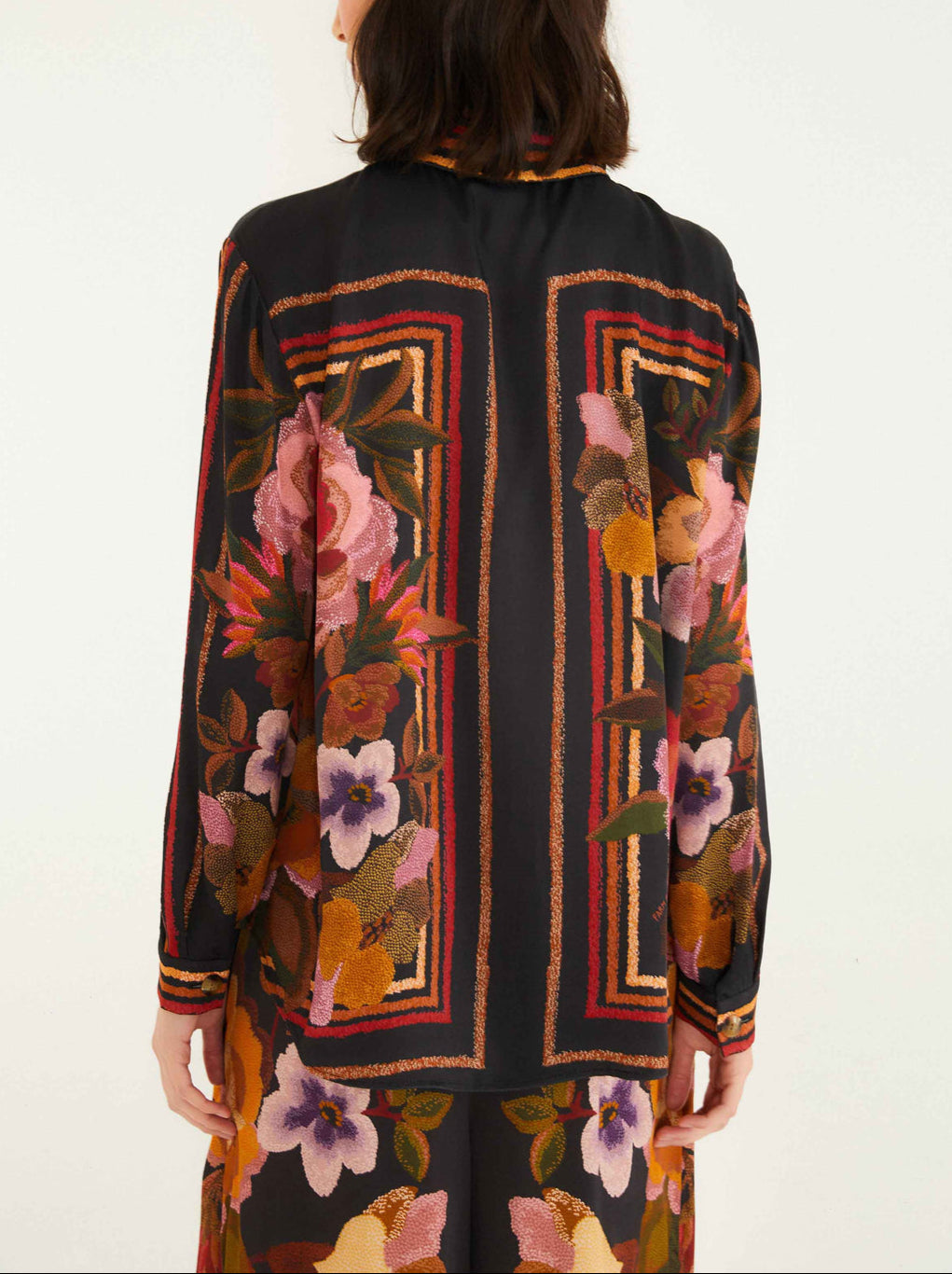 A woman is seen from behind wearing the Farm Rio Chenille Flowers Black Shirt, a long-sleeved top with a vibrant floral and geometric pattern made from eco-conscious viscose.