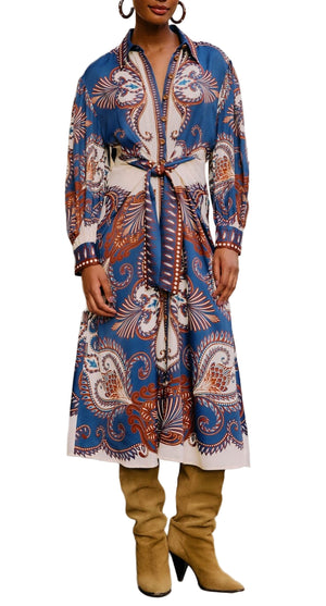 Woman wearing the Farm Rio Arabesque Scarf Blue Midi Dress, a long-sleeve, button-down midi with blue, white, and brown paisley patterns, a belted waist, paired with tan knee-high boots.